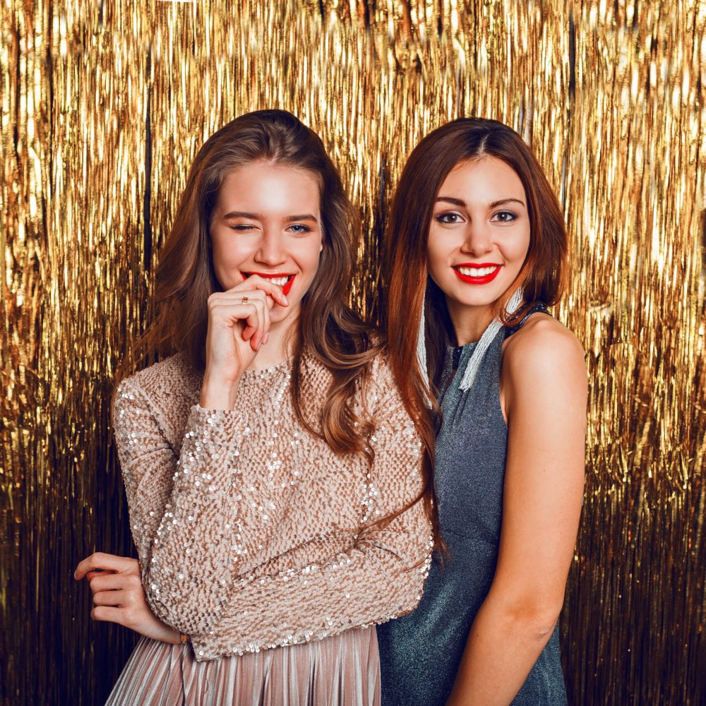 Close up studio image of two amazing sexy celebrating girls  with red lips, surprise face, laughing , posing on golden sparkly background. New year party mood.